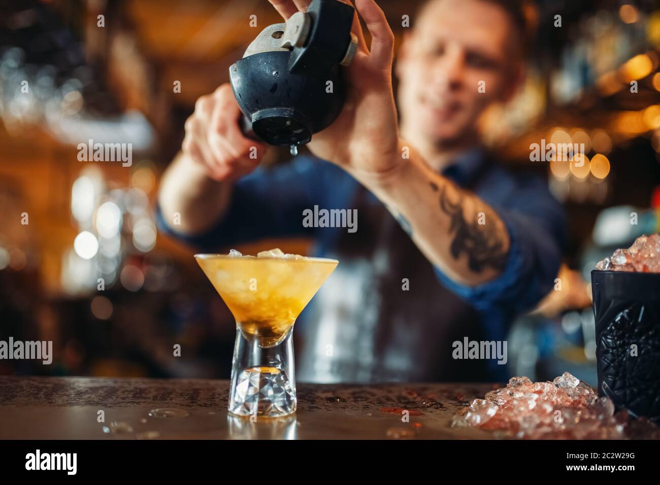 Male barman squeezes lemon into the glass full of ice. Barkeeper occupation, bartender at the bar counter Stock Photo