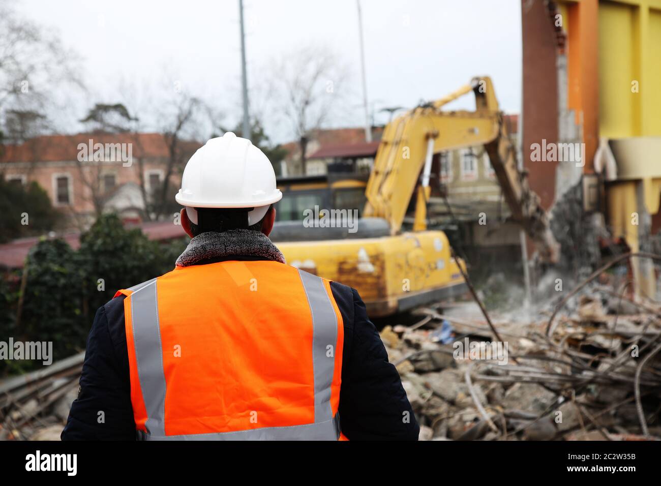 Engineer mans in helmet and jacket controlling outdoor construction site. Engineer man watching machinery on demolition site. Stock Photo