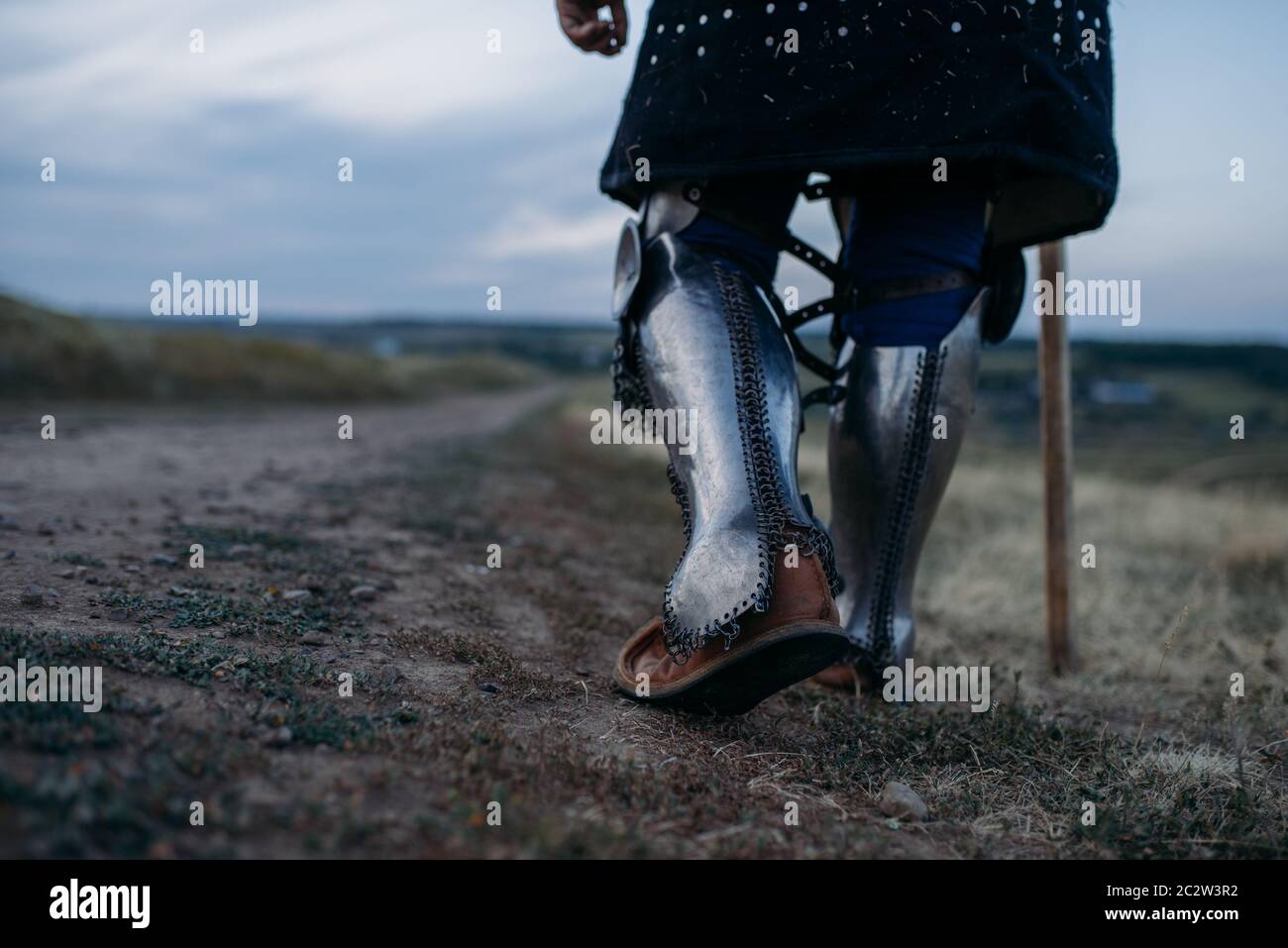 Medieval knight legs in metal armor, back view, great tournament. Armored ancient warrior in armour posing in the field Stock Photo