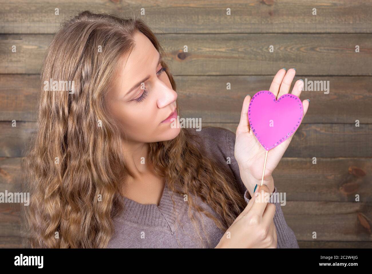 Young woman with funny pink heart in hand, wooden background. Fun photo props and accessories for shoots Stock Photo