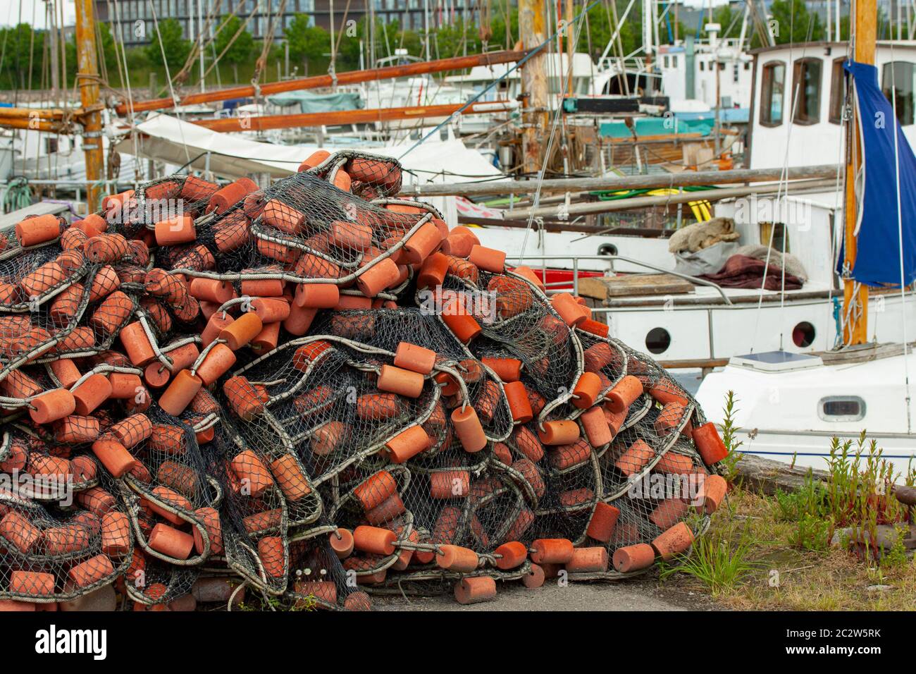 Pile of fishing net with floaters on a harbor and fishing boats in the background. Stock Photo