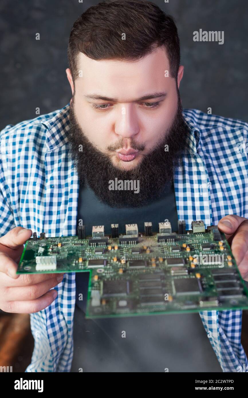 Male computer engineer blows off the dust from motherboard. Electronic ...
