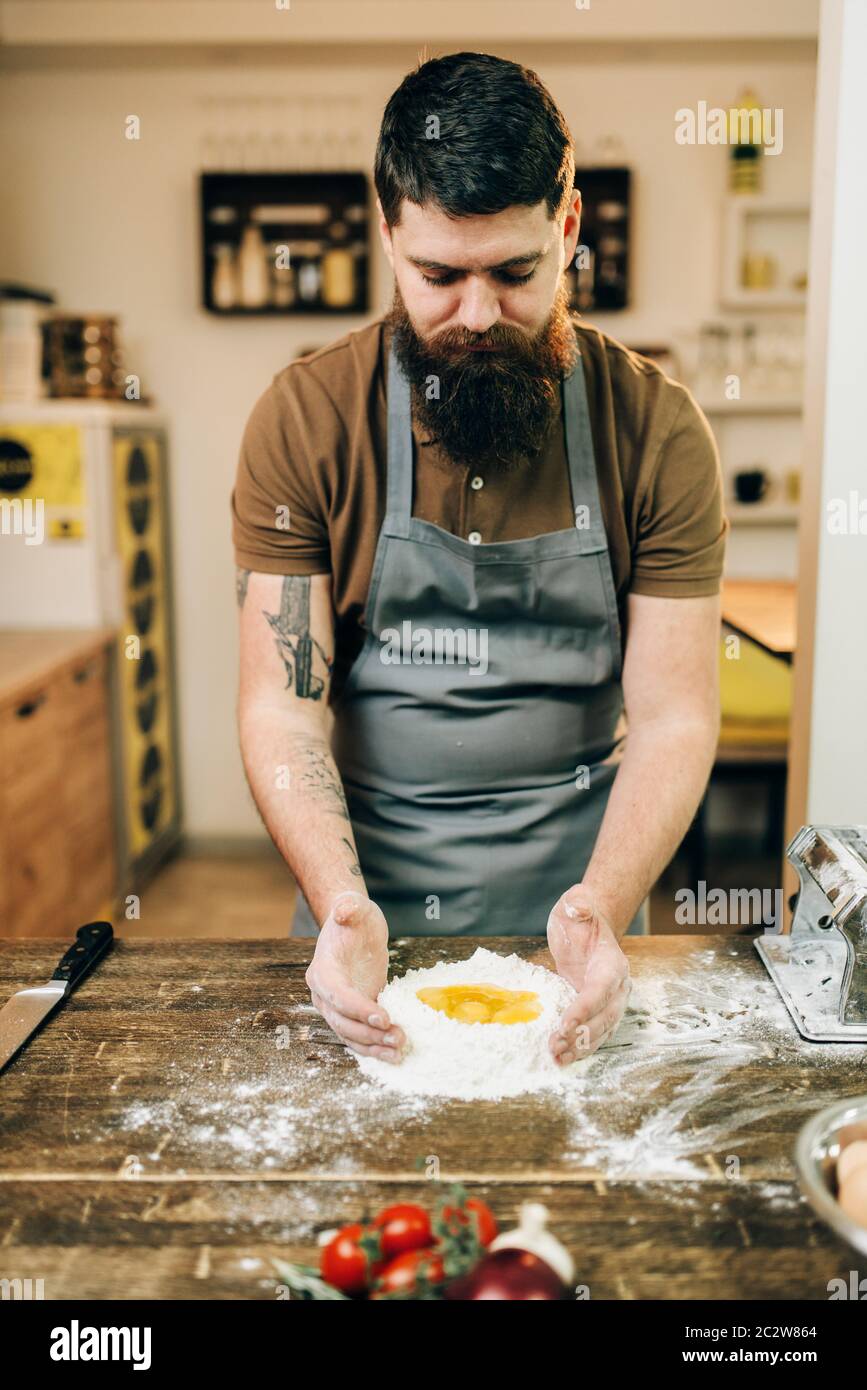 Homemade pasta cooking, bearded chef preparing dough on wooden kitchen table Stock Photo