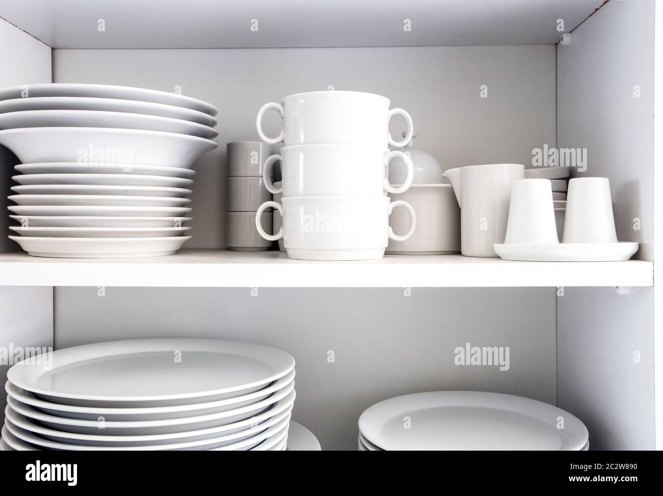 White Cupboard with white crockery in the kitchen, various clean dishes close-up Stock Photo