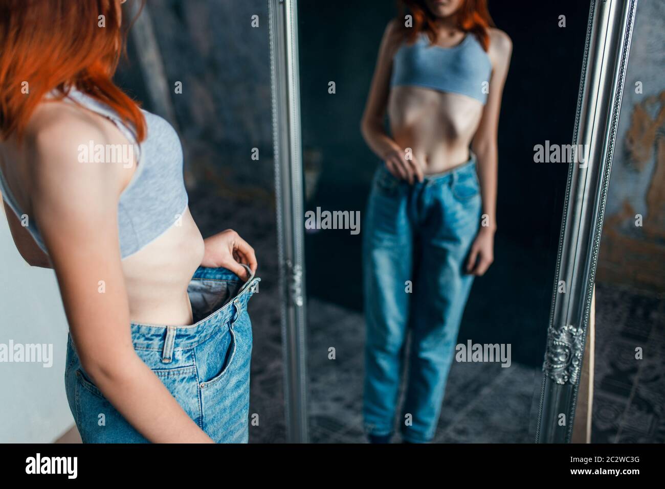 Thin woman tries on big size jeans against mirror, weight loss, anorexia. Fat or calories burning concept, medical illness Stock Photo