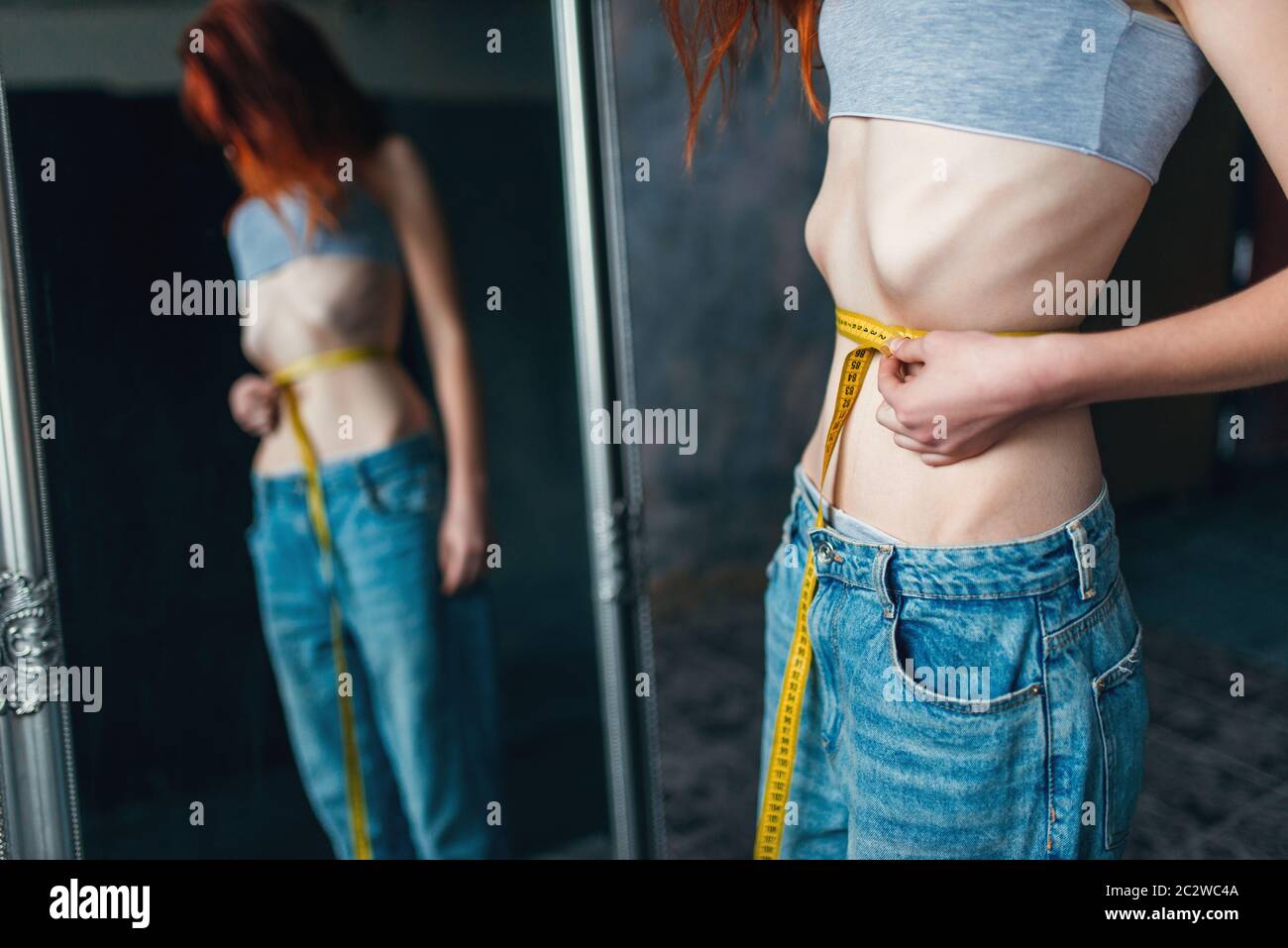 Thin woman measures her waist against mirror, weight loss, anorexia. Fat or calories burning concept, medical illness Stock Photo