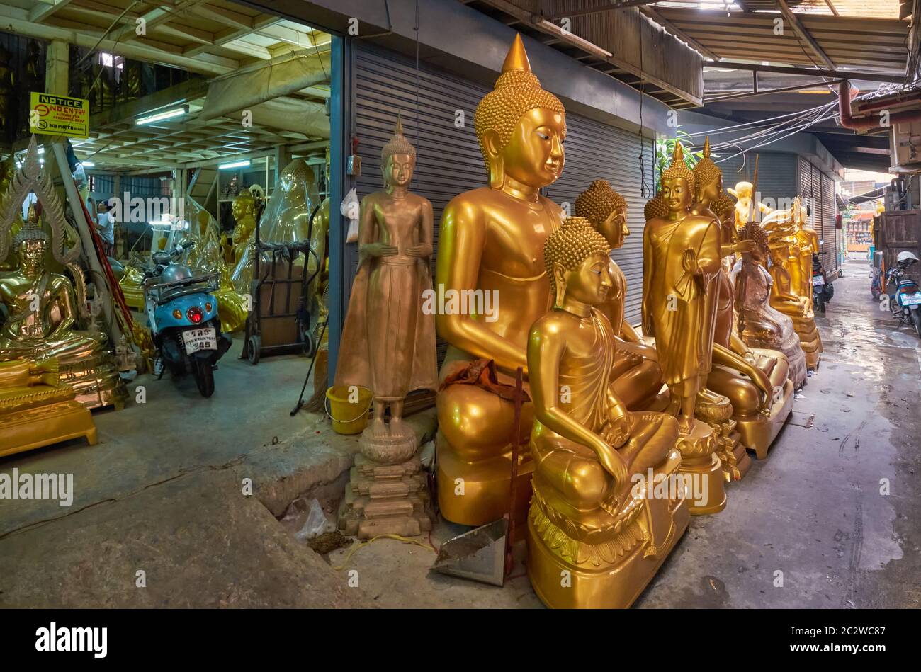Buddha statues stand in front of a factory for Buddha statues and other religious objects in a side lane off Bamrung Muang Road, Bangkok, Thailand Stock Photo