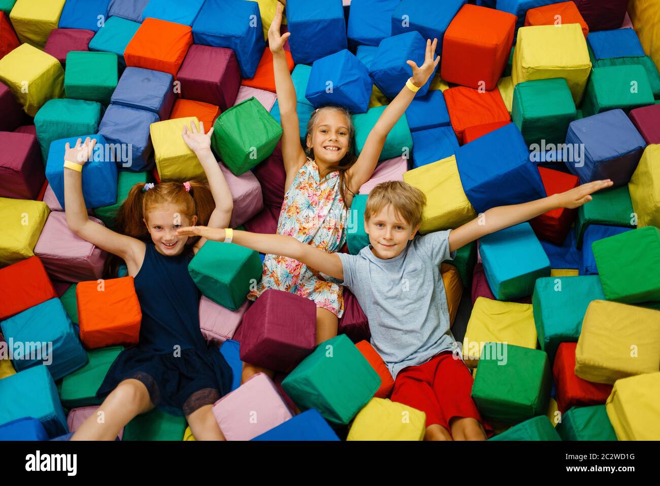 Happy children lying in soft cubes, playground in entertainment center. Play area indoors
