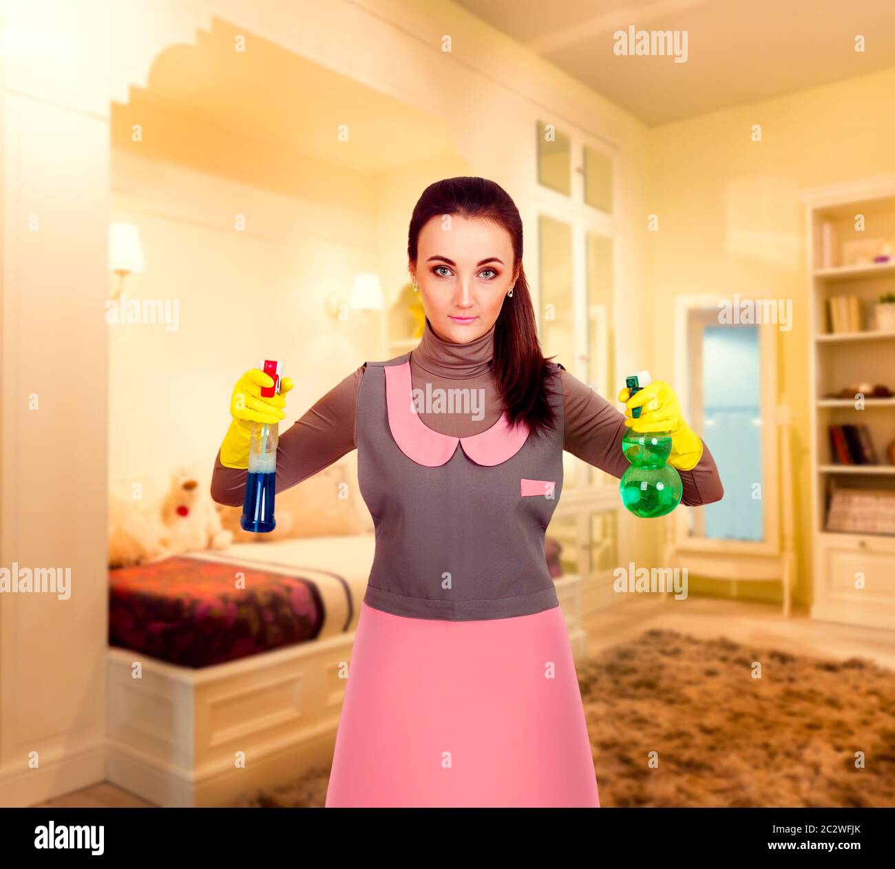 Young housemaid woman in uniform and rubber gloves cleaning the room ...