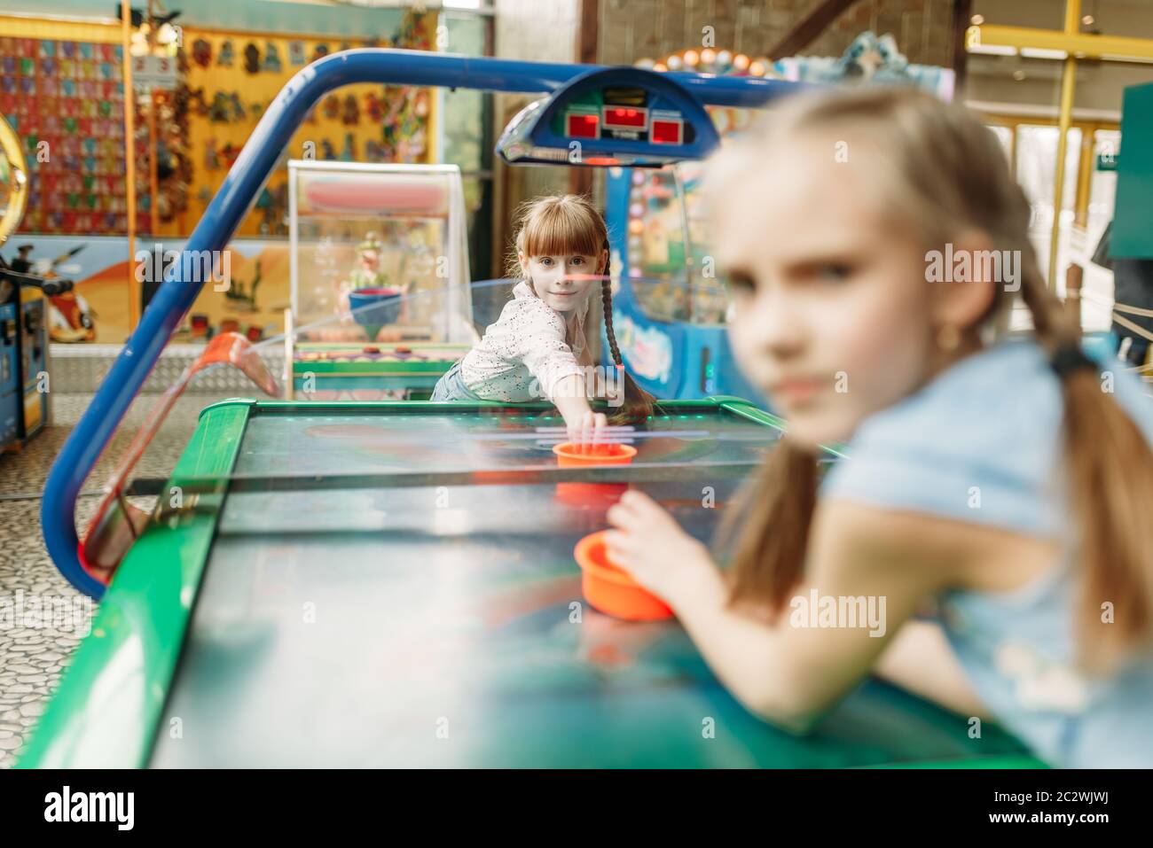 Two little girls plays air hockey in children game center. Excited childs having fun on