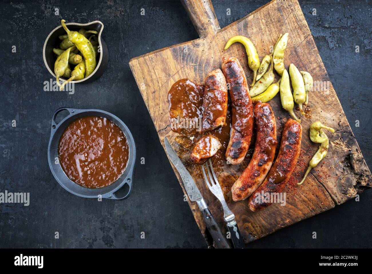Traditional barbecue German Bratwurst with hot sauce and peperoni as top view on an old cutting board with copy space Stock Photo