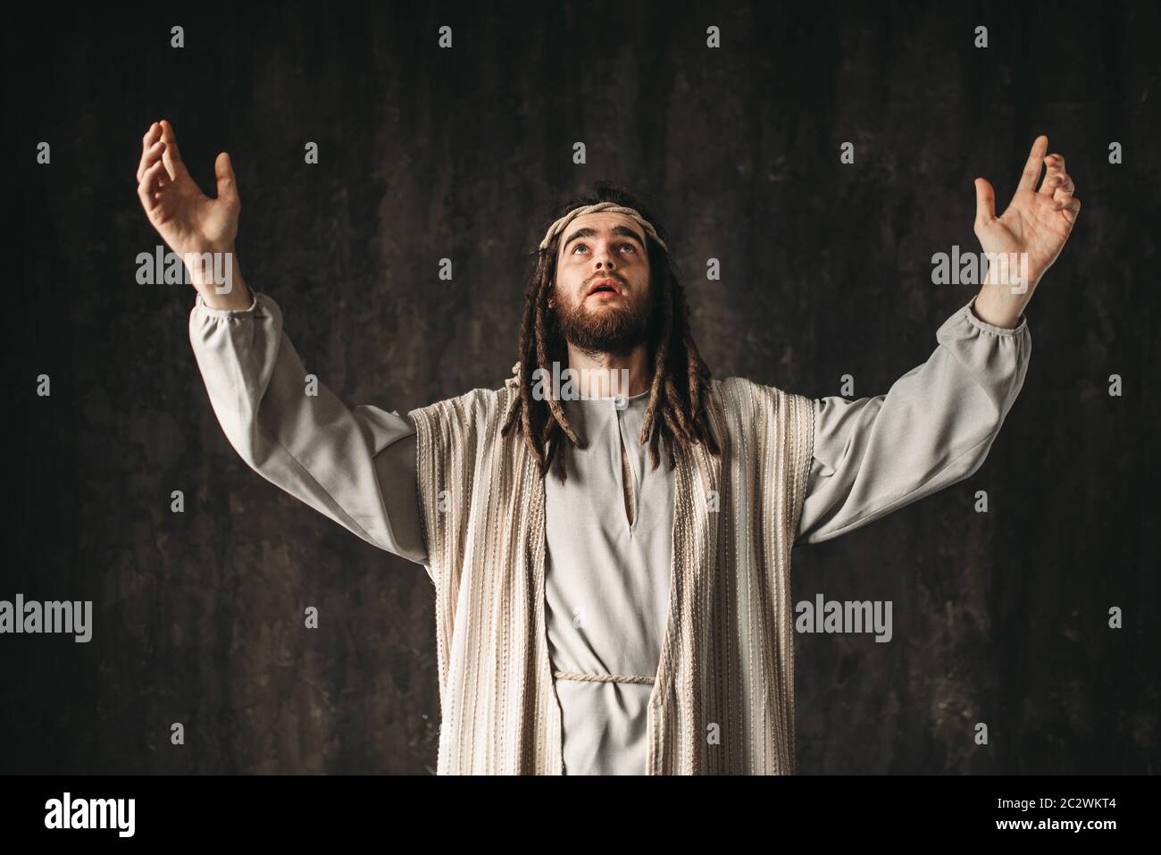 Jesus Christ in white robe emotionally prays with his hands up, dark ...