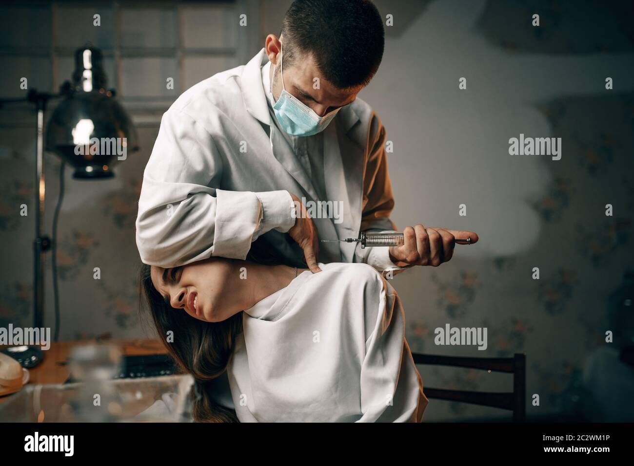 Psychiatrist with syringe makes a sedative injection to crazy female patient, mental hospital. Woman undergoing treatment in clinic for the mentally i Stock Photo