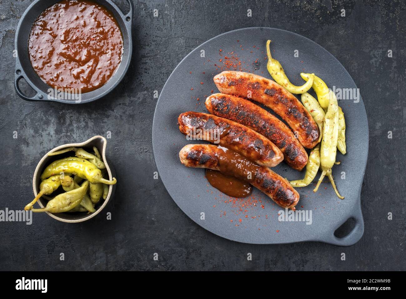 Traditional barbecue German Bratwurst with hot sauce and peperoni as top view on a modern design cast iron plate Stock Photo