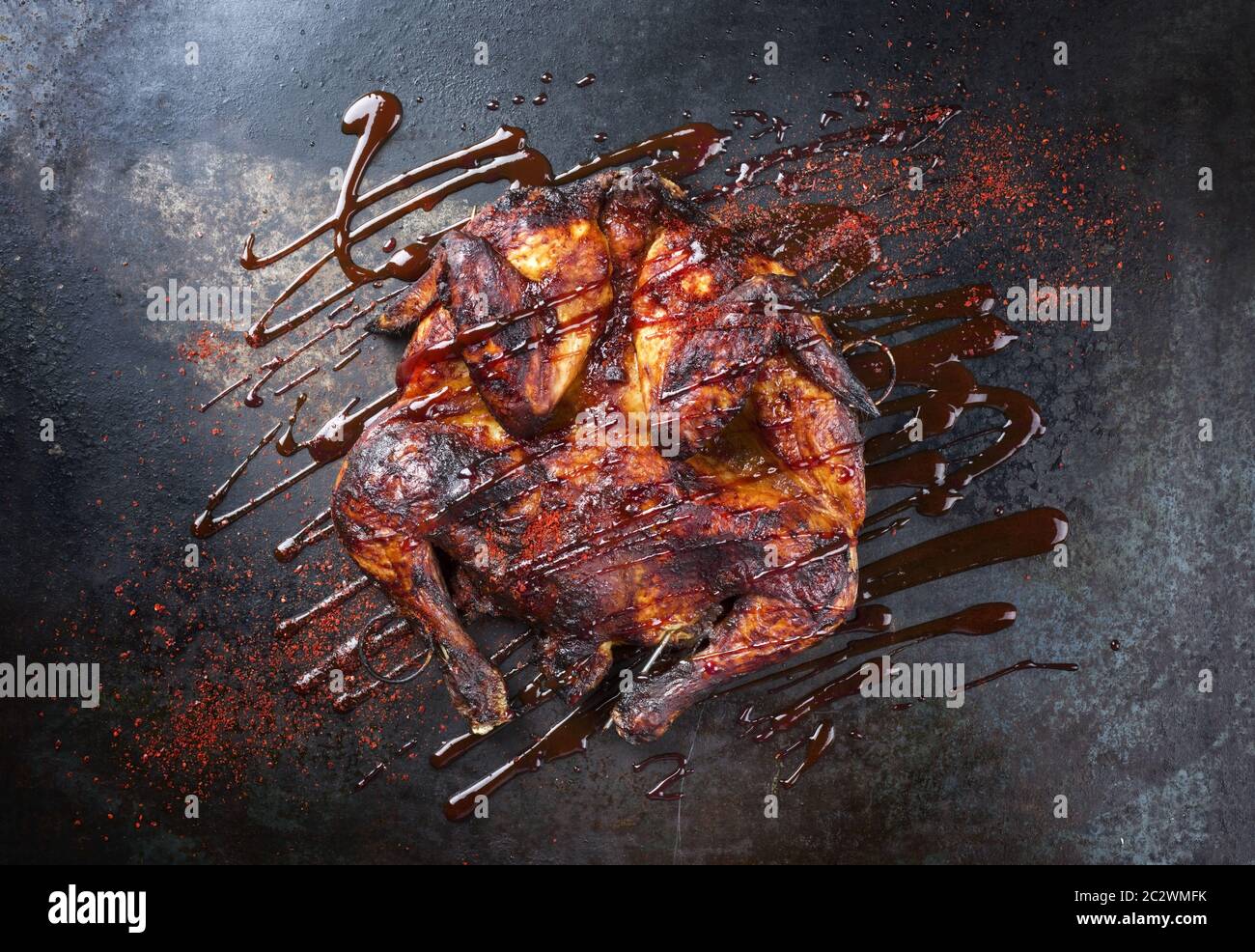 Barbecue spatchcocked barbecue chicken al mattone with hot chili sauce as top view on an old metal sheet Stock Photo