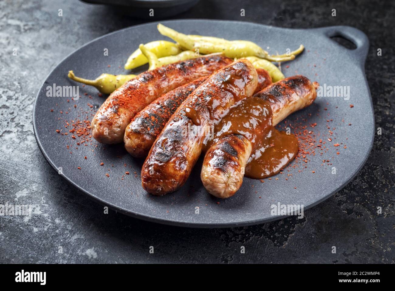 Traditional barbecue German Bratwurst with hot sauce and peperoni as closeup on a modern design cast iron plate Stock Photo