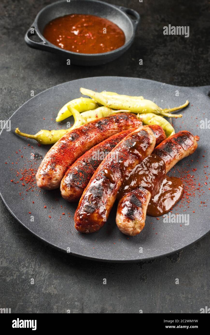 Traditional barbecue German Bratwurst with hot sauce and peperoni as closeup on a modern design cast iron plate Stock Photo