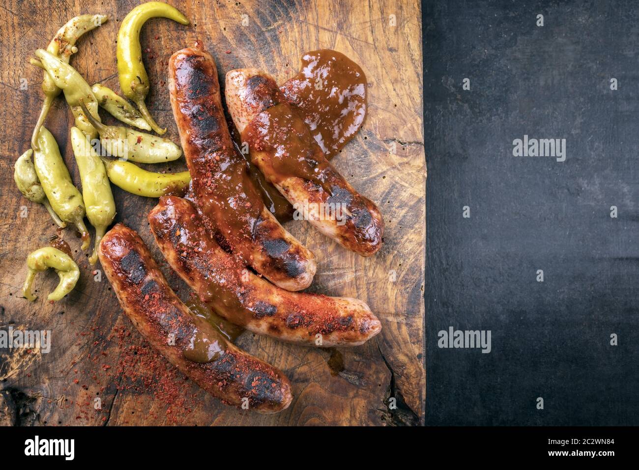 Traditional barbecue German Bratwurst with hot sauce and peperoni as top view on an old cutting board with copy space right Stock Photo
