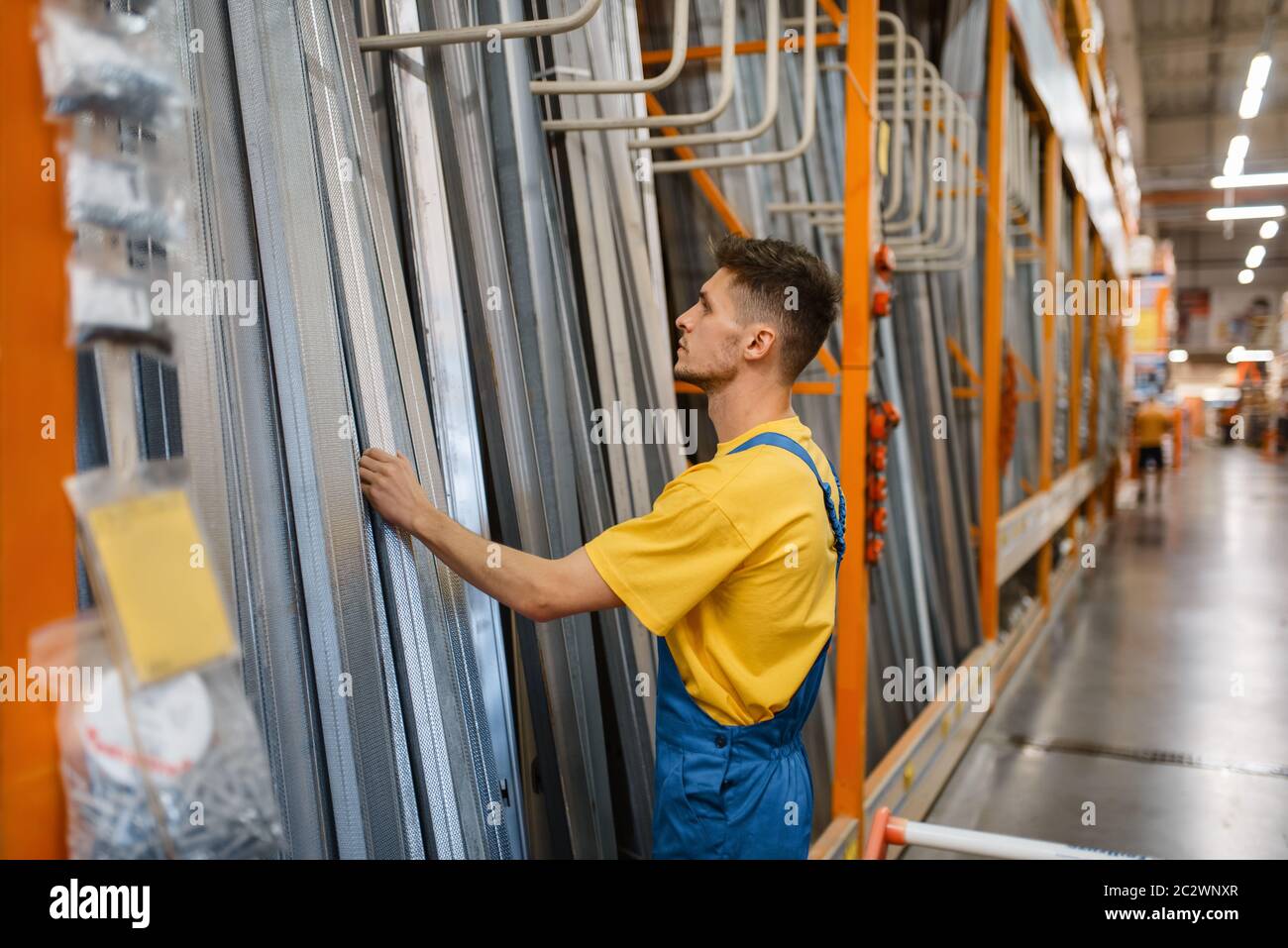 Male constructor choosing repair materials in hardware store. Builder in uniform look at the goods in diy shop Stock Photo