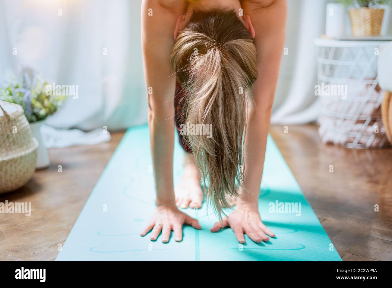 Close up Young attractive sporty woman practicing yoga, standing forward bend exercise, head to knees, uttanasana pose, working out at home in living Stock Photo