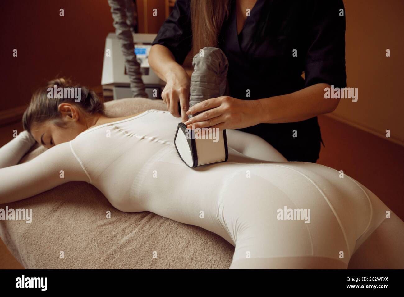 Female masseur with vibrating massager and young woman in massage suit  relaxing on the table. Massaging and relaxation, body and skin care.  Attractive Stock Photo - Alamy