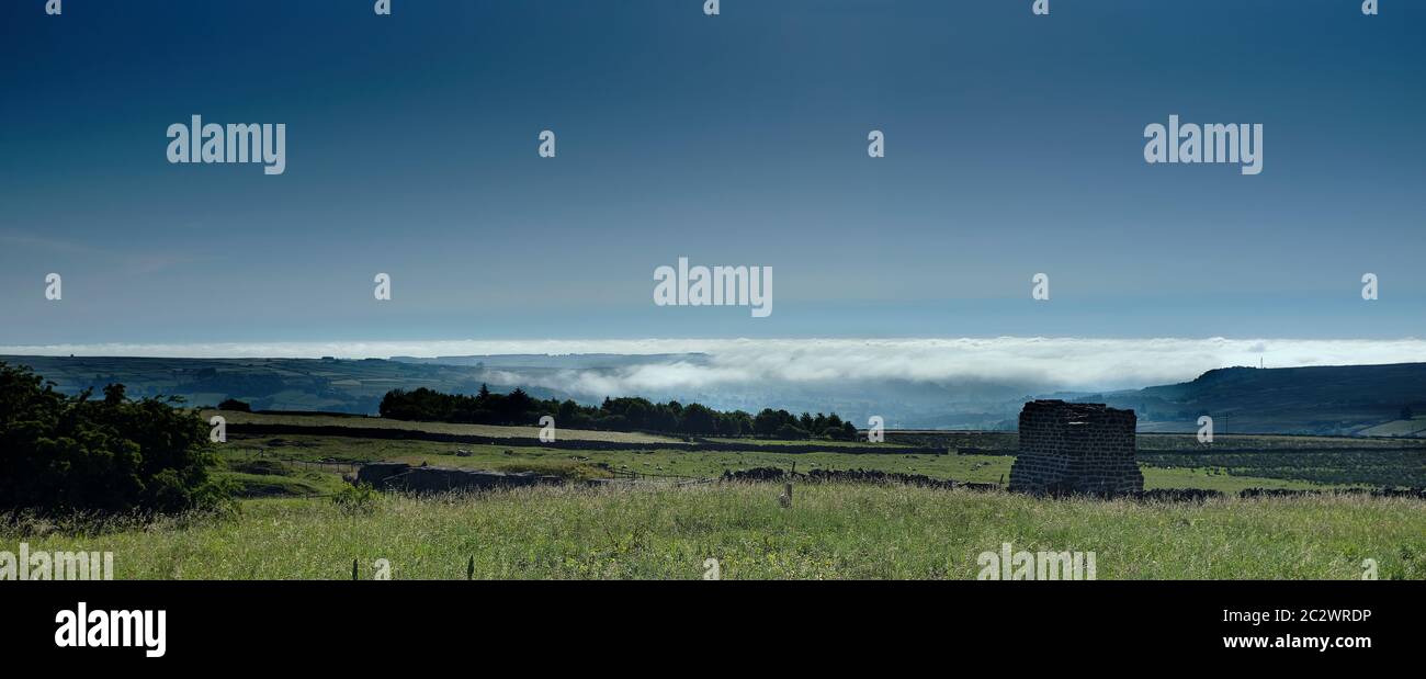 Late June, and morning clouds hang over Nidderdale looking east from Greenhow Hill. Historic remains of lime kiln chimney in the foreground Stock Photo