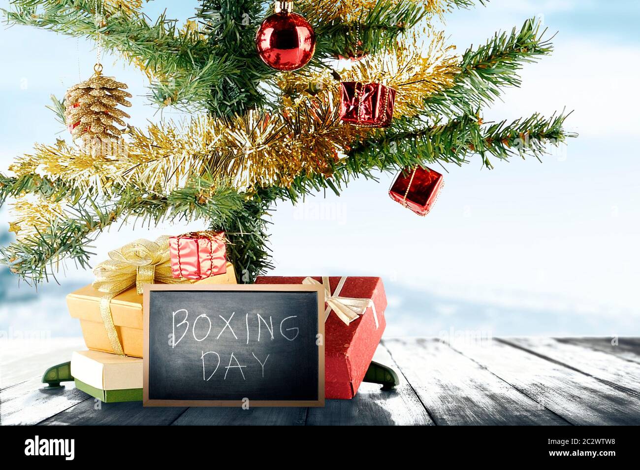 Christmas tree with gift box and Boxing Day text on the blackboard on wooden floor with a snowy background Stock Photo