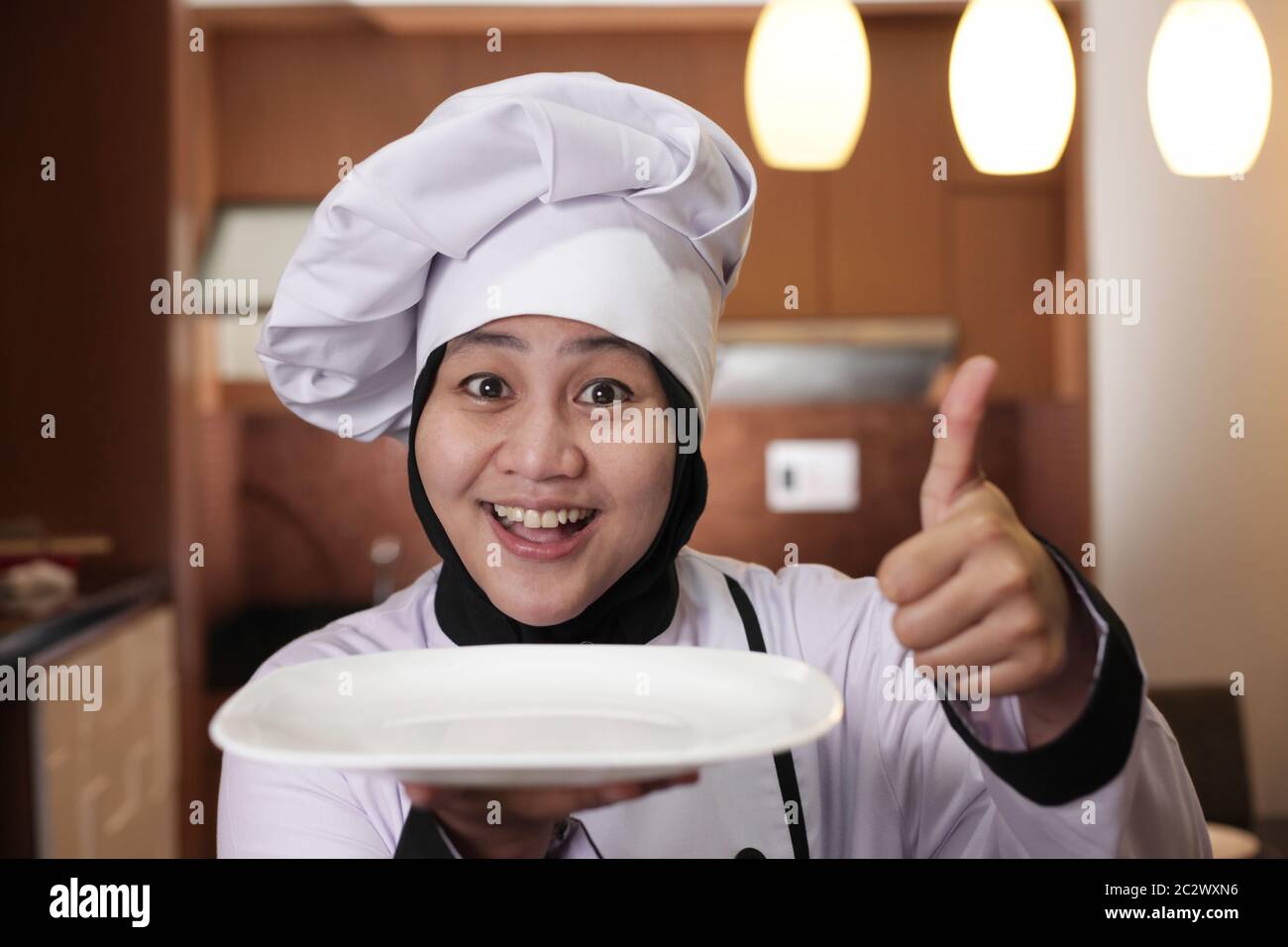 Portrait of Asian female chef looks happy and proud presenting something on her empty white plate, copy space meal menu concept Stock Photo