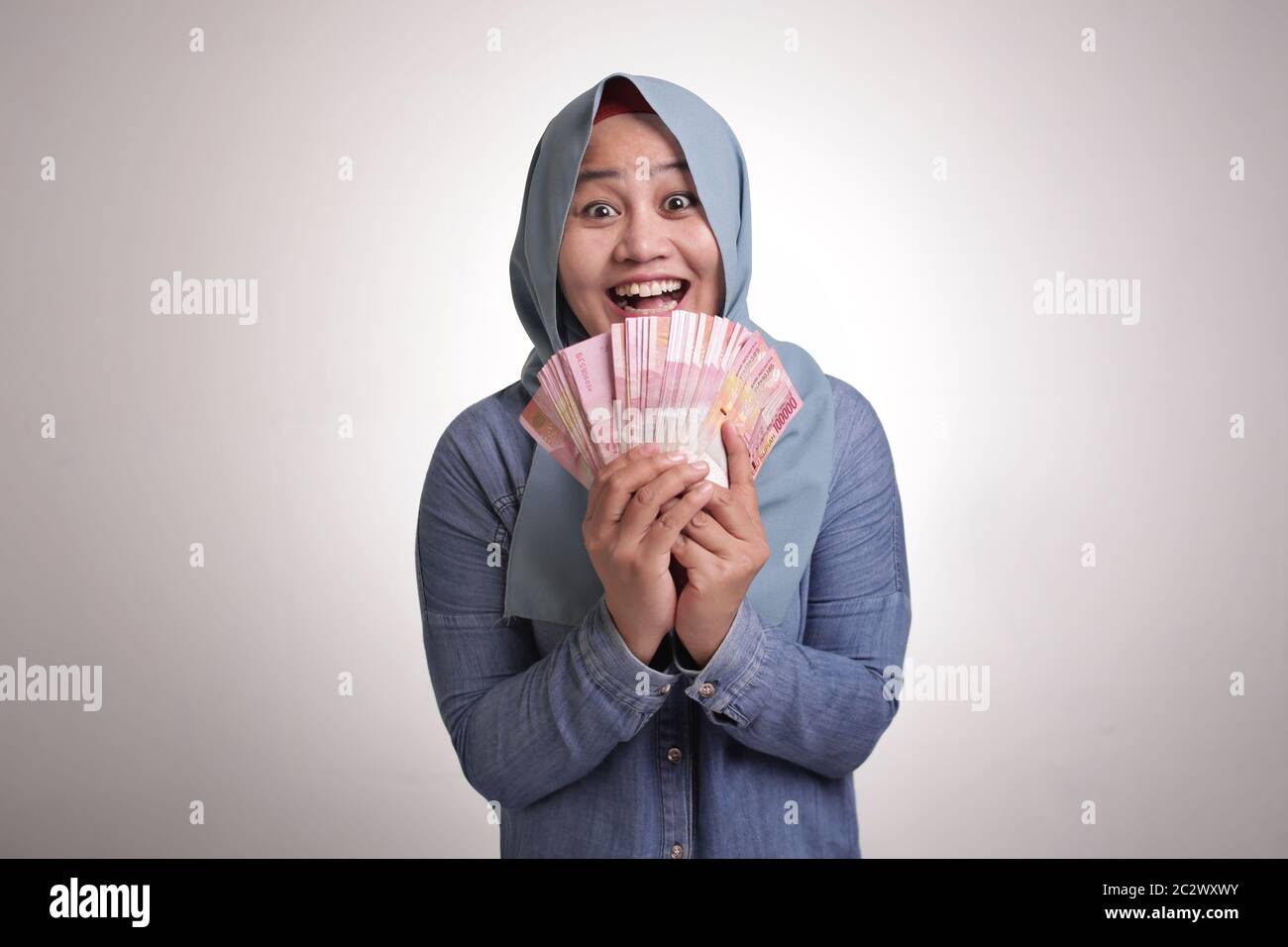 Portrait of Indonesian muslim woman holding rupiah money, smiling laughing winning gesture Stock Photo
