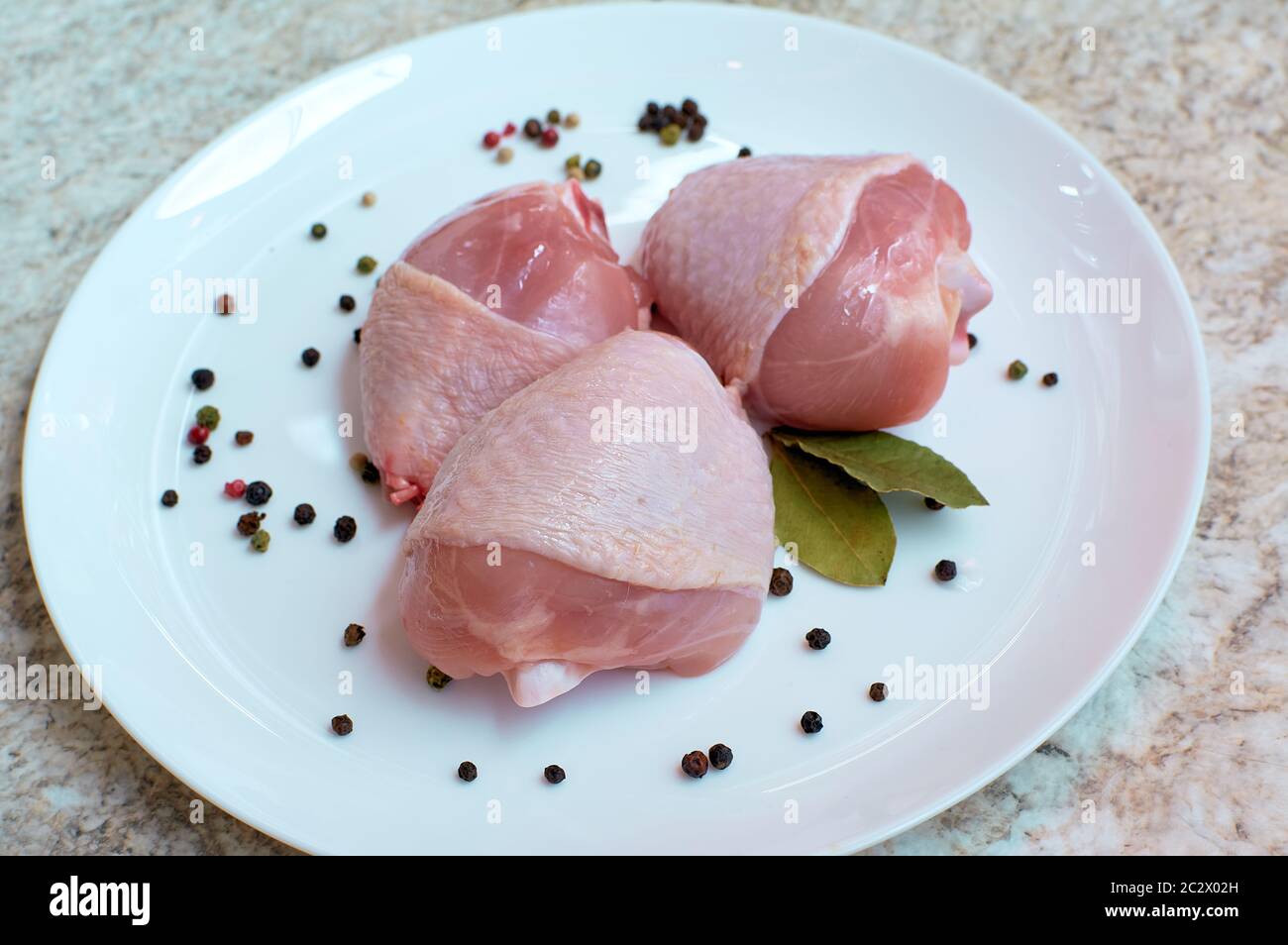 Fresh raw chicken thighs on a white plate. Flowered allspice and bay leaf Stock Photo