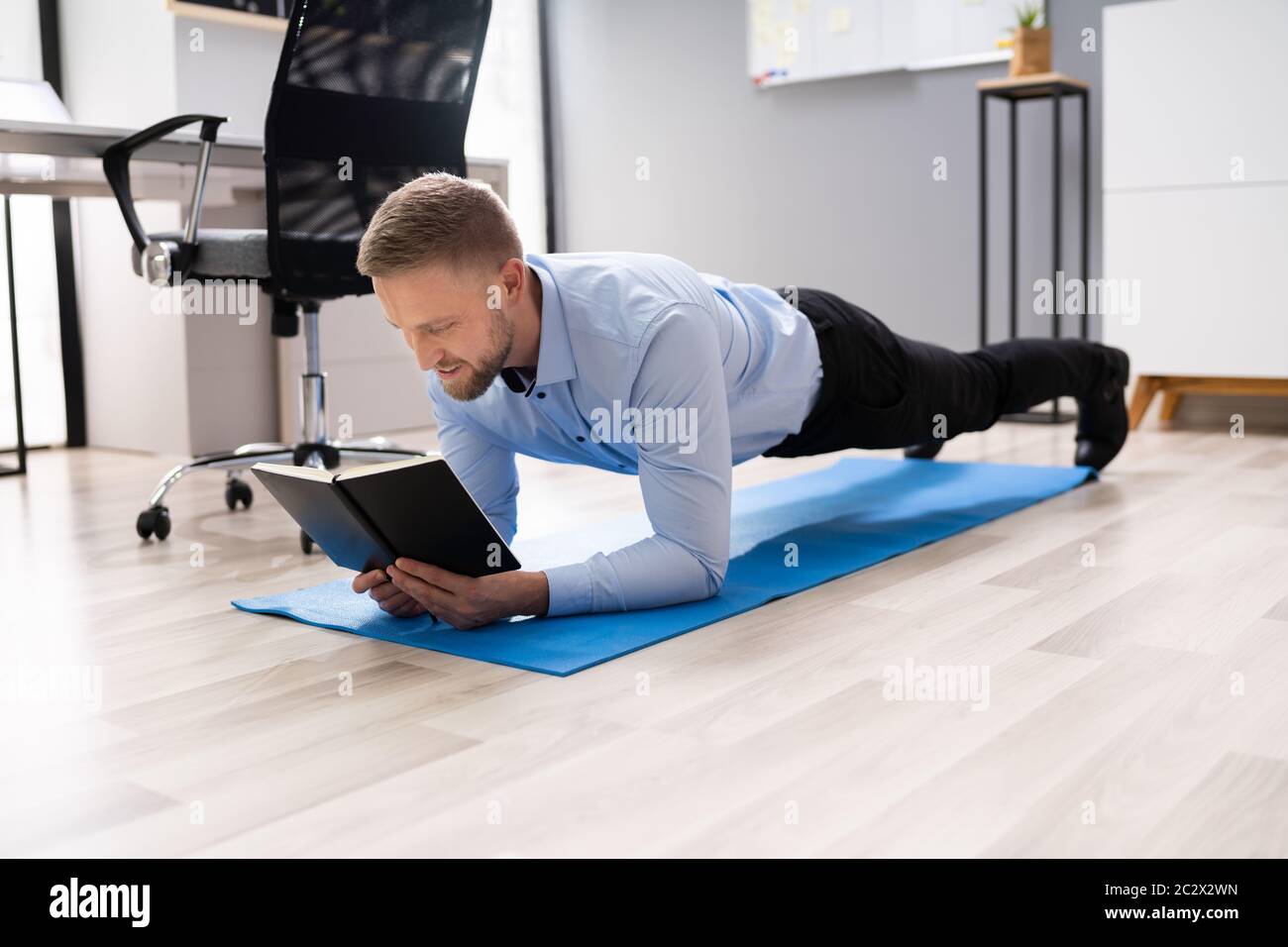 Businessman Reading Notes While Doing Plank Exercise In Office Stock Photo