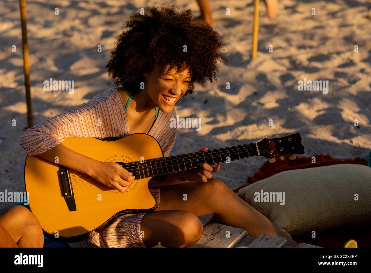 Young mixed race woman playing guitar and laughing on beach Stock Photo