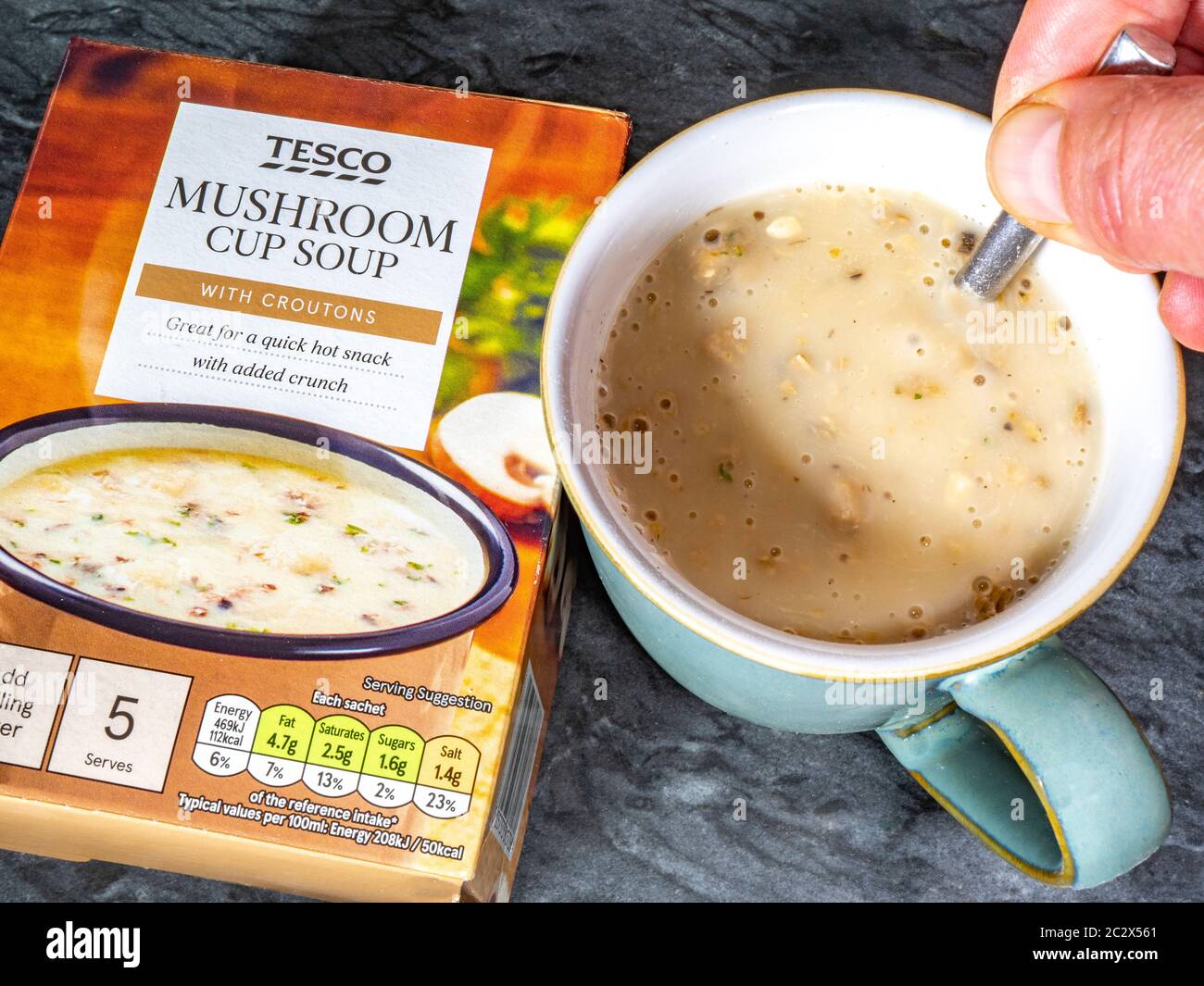 Tesco own brand mushroom soup with croutons – a product box and a sachet of dry soup mixed with with boiling water, being stirred in a cup. Stock Photo