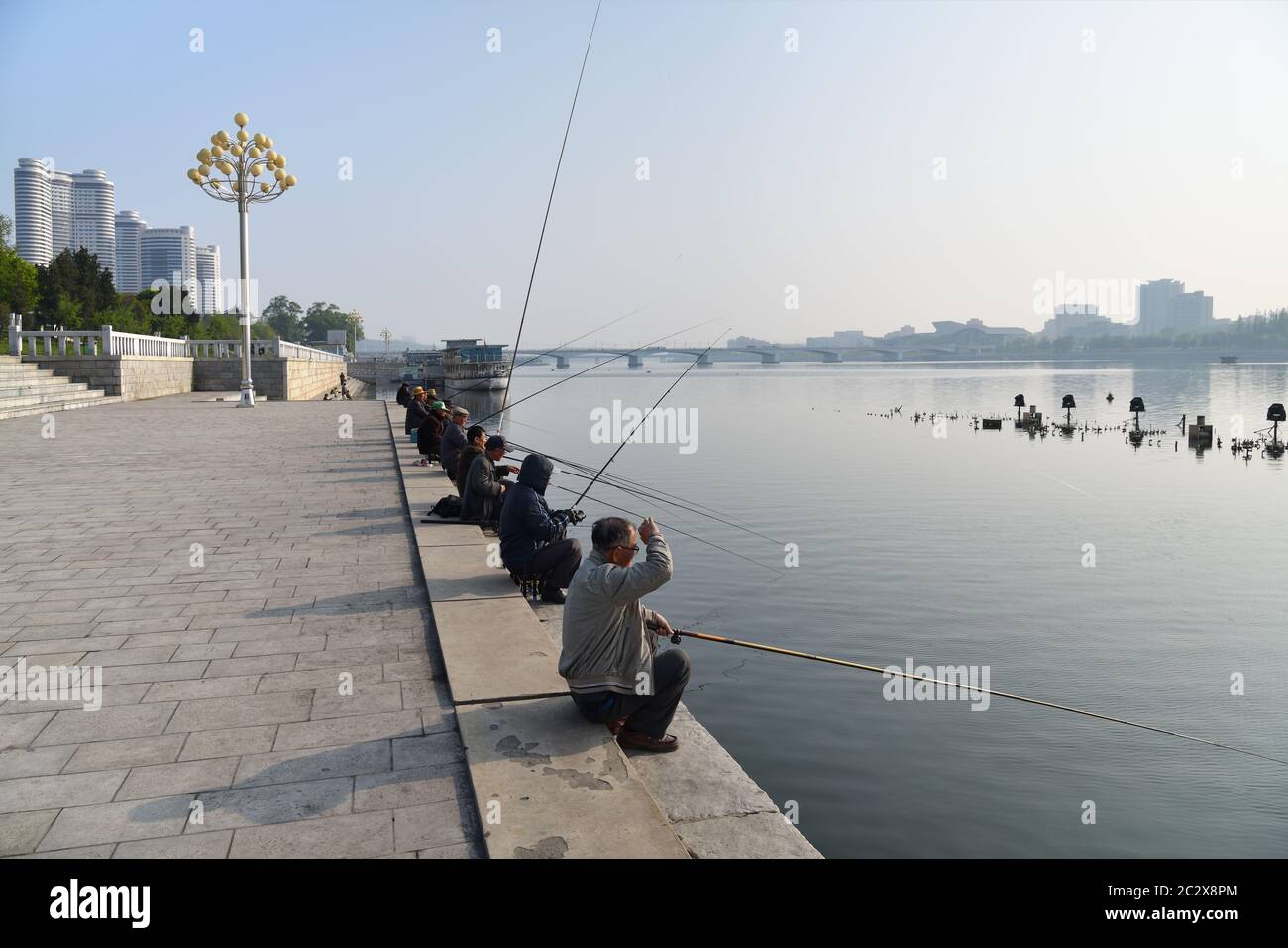Pyongyang, North Korea - May 1, 2019: Locals fishermen catch a fish on waterfront on Kim Il Sung square at the morning Stock Photo
