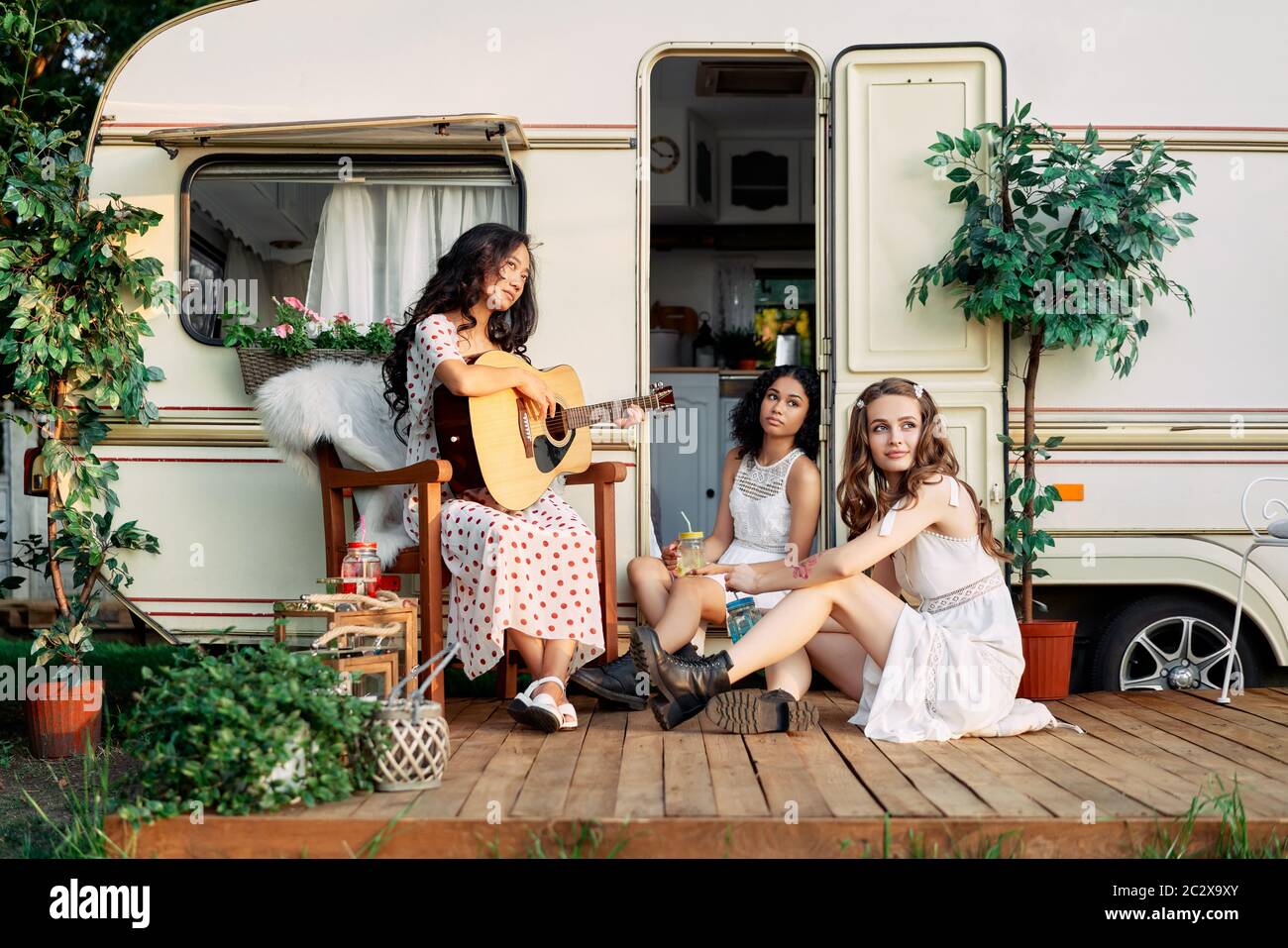 Laughing happy women with guitar have fun together outdoors near their camper van during summer travel Stock Photo