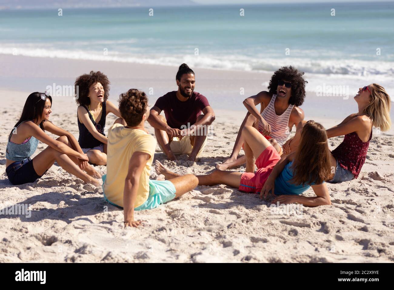 Multi-ethnic group of male and female sitting on the beach Stock Photo