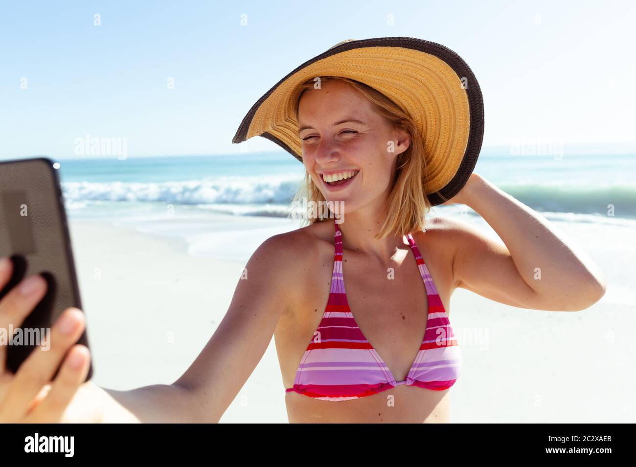 Caucasian woman at beach wearing a hat and taking selfie with her smartphone Stock Photo