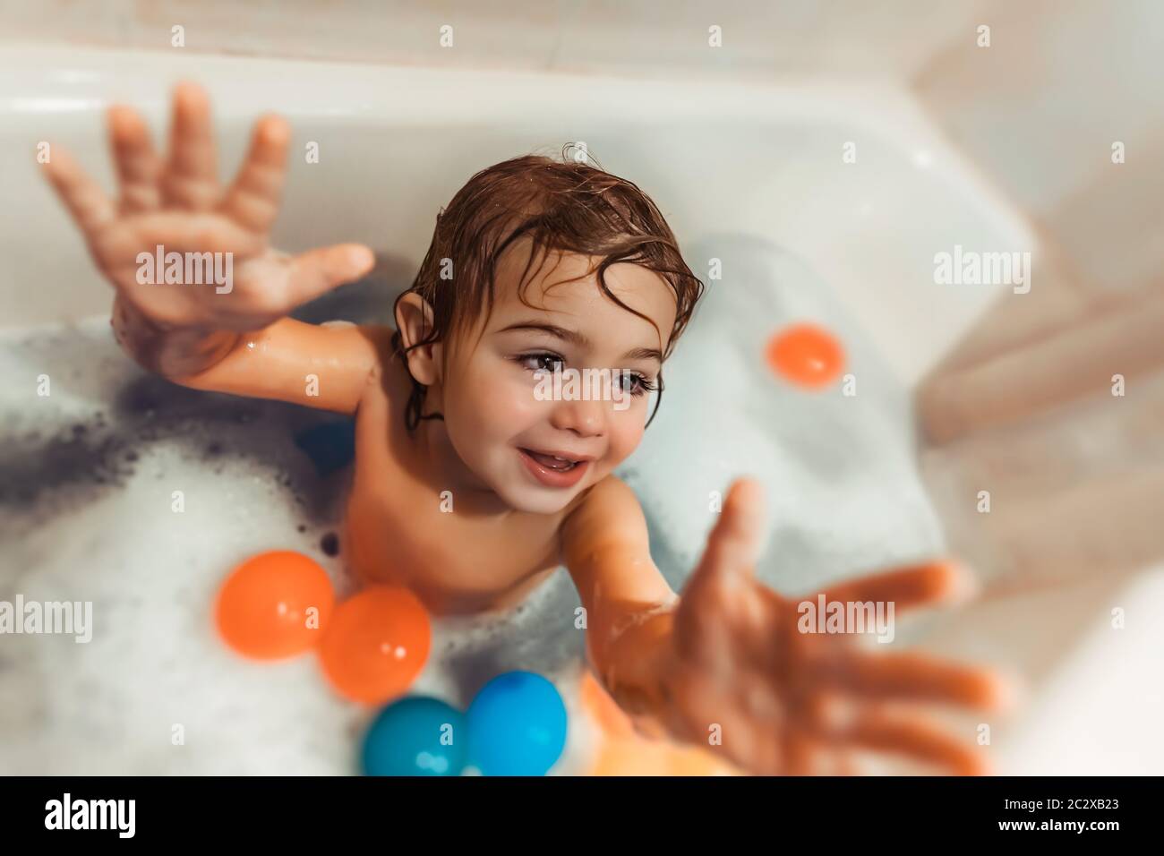 Cheerful boy taking bath, little child with pleasure bathing with foam