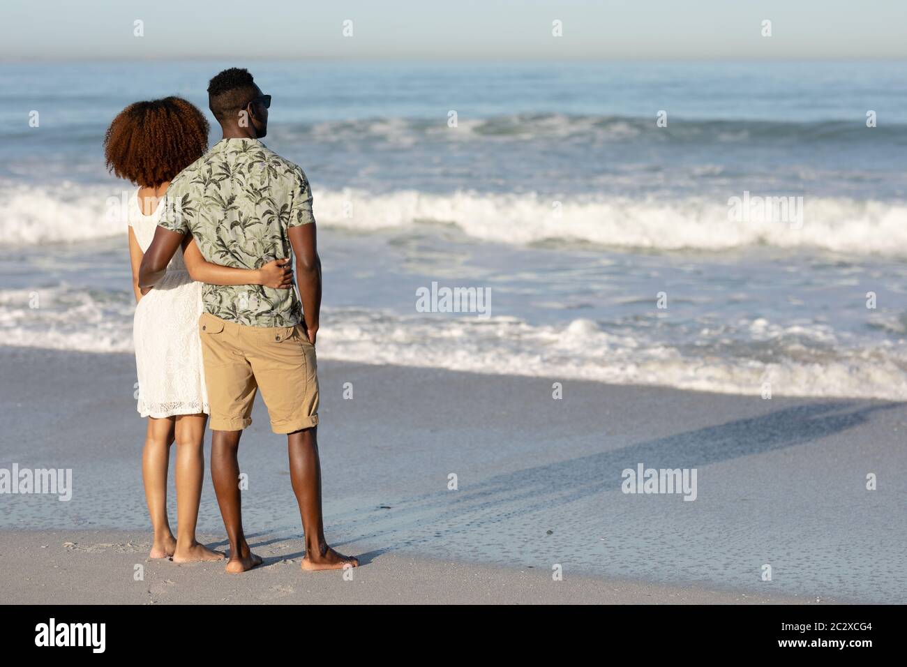 A mixed race couple admiring the view and holding each other on beach Stock Photo