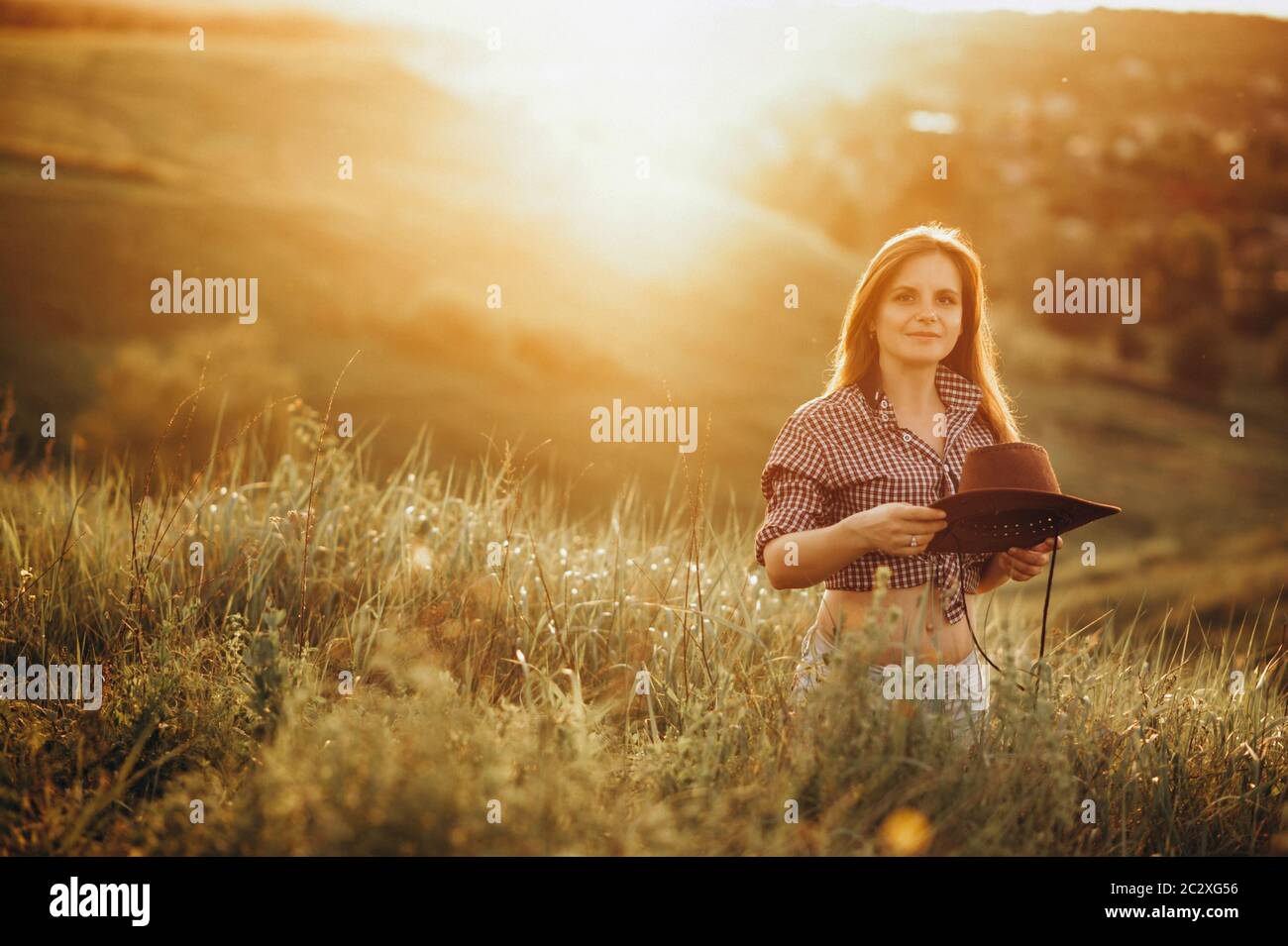 Girl in American country style, shirt and cowboy hat at nature. On the Sunset Stock Photo