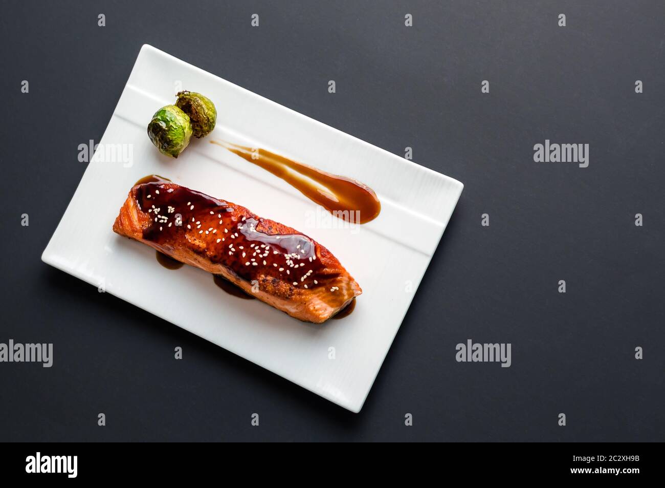 Japanese cuisine inspired food made of grilled salmon fillet glazed in delicious teriyaki sauce (soy sauce base) & Brussels sprouts on white plate. Stock Photo