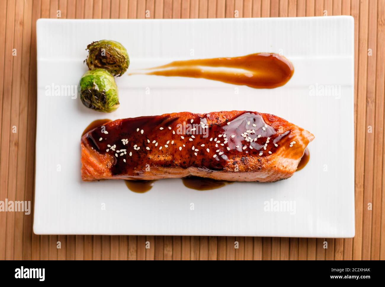 Japanese cuisine inspired food made of grilled salmon fillet glazed in delicious teriyaki sauce (soy sauce base) & Brussels sprouts on white plate. Stock Photo