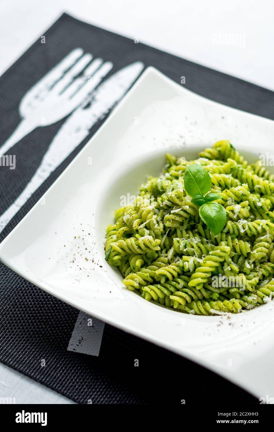 Basil pesto pasta vertical. Rotini pasta with basil pesto sauce, grated parmesan cheese and fresh pepper. This Italian dish makes a delicious meal. Stock Photo