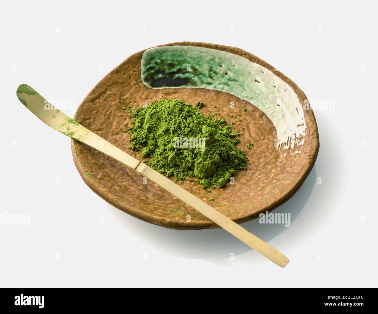 Japanese matcha green tea powder on a ceramic clay plate with a chasaku bamboo spoon (used to scoop the maccha in a bowl during tea ceremony) on white Stock Photo
