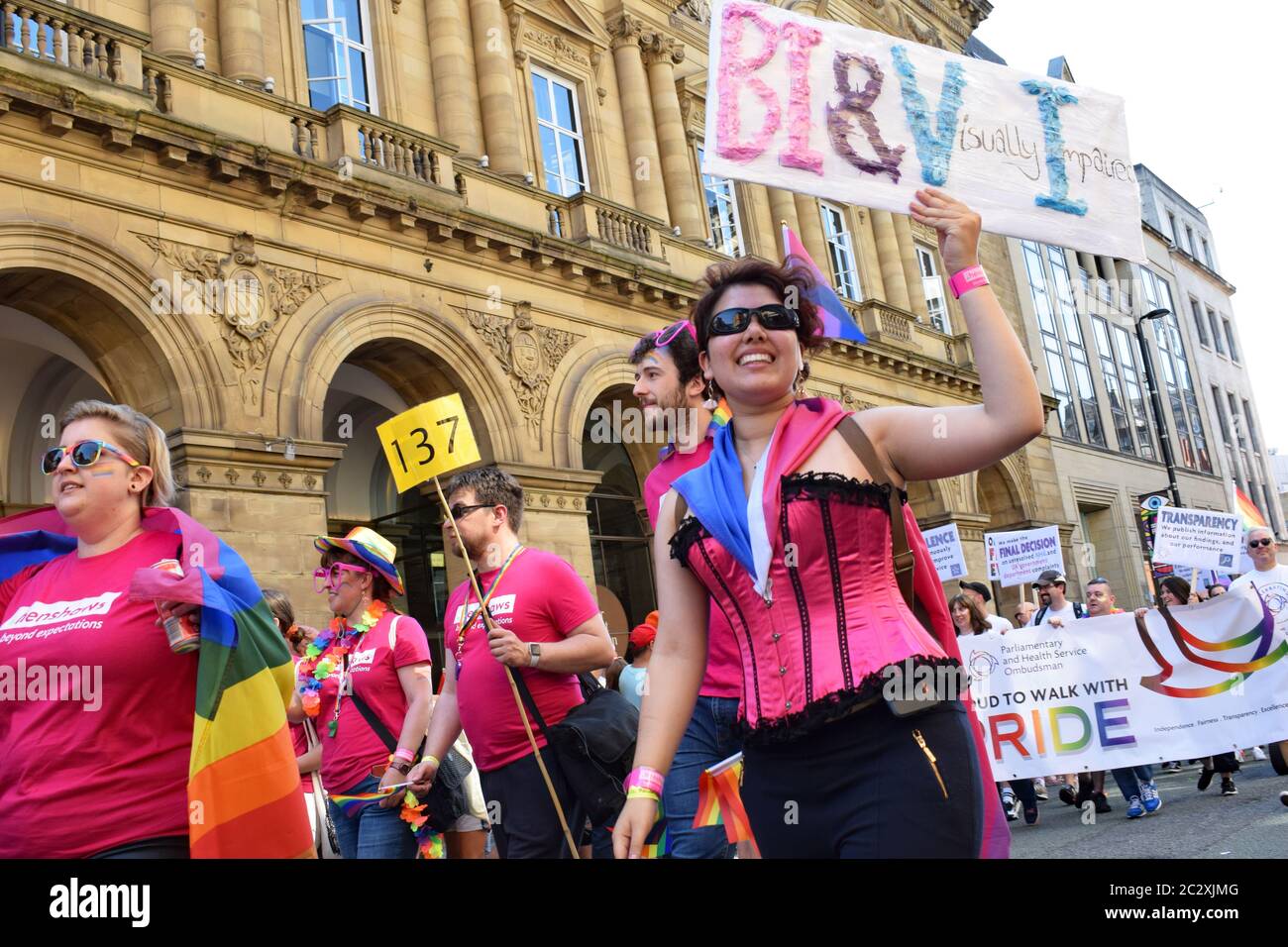 Pride parade Manchester passing in front of Radisson Hotel on Peter Street Visually impaired woman in pink basque in procession holding sign BI&VI Stock Photo