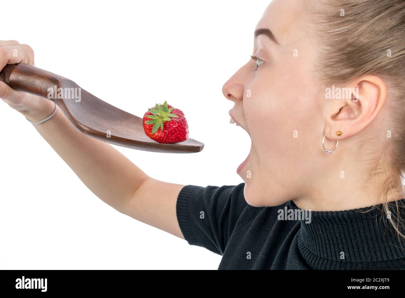 young vegetarian woman is holding a huge spoon with a strawberry on it to eat it Stock Photo