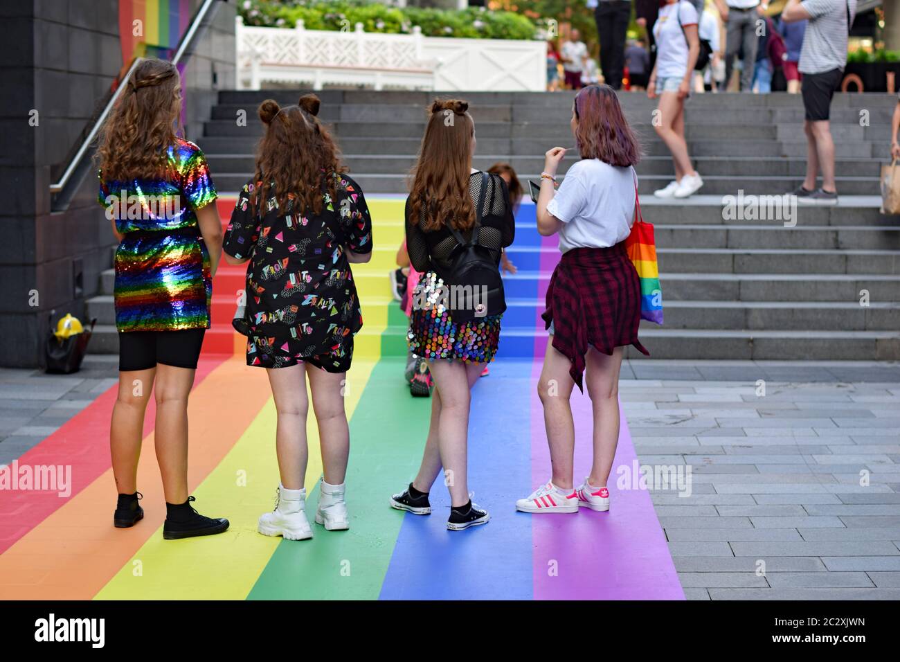 Four women standing on rainbow artwork painted floor on steps in Spinningfields Manchester during pride weekend Stock Photo