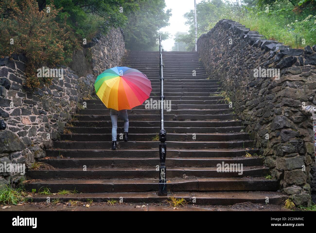 Woman with colourful umbrella climbs steps at Calton Hill on rainy day, Edinburgh, Scotland, UK Stock Photo