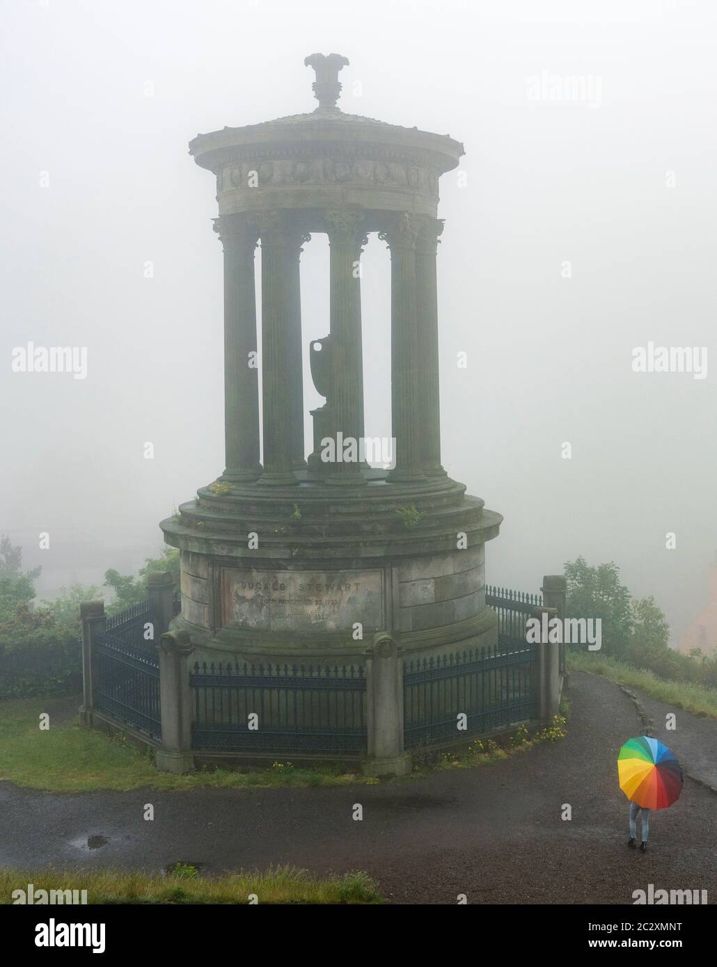 Woman with colourful umbrella and Dugald Stewart monument Calton Hill on foggy , rainy day, Edinburgh, Scotland, UK Stock Photo