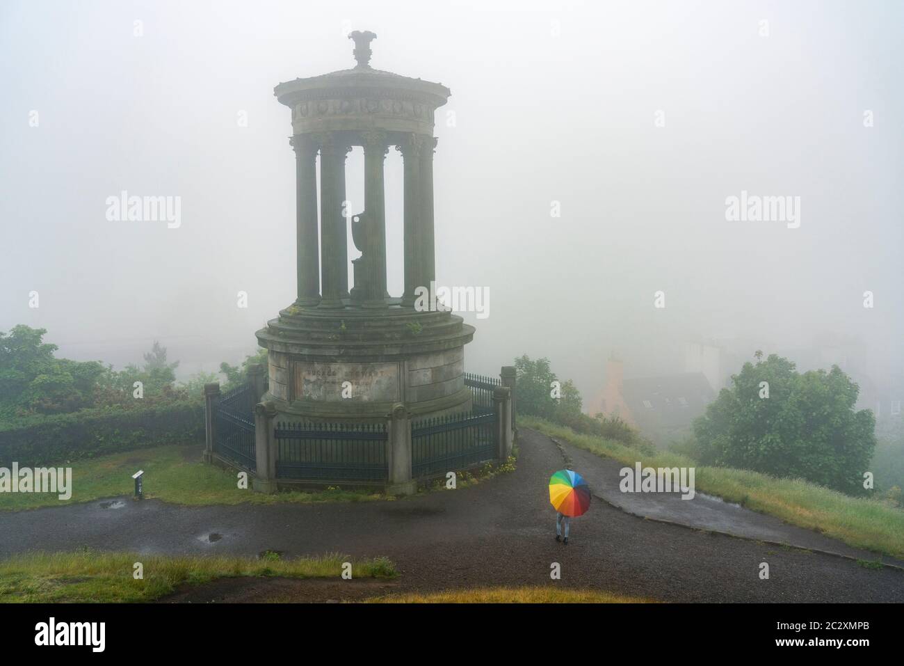 Woman with colourful umbrella and Dugald Stewart monument Calton Hill on foggy , rainy day, Edinburgh, Scotland, UK Stock Photo